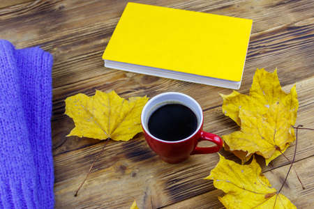 Cozy knitted blue sweater, book, cup of coffee and autumn maple leaves on wooden table. autumn cozy conceptの写真素材