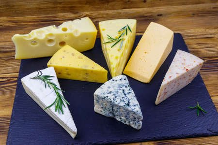 Set of various types of cheese on black slate board on a wooden tableの写真素材
