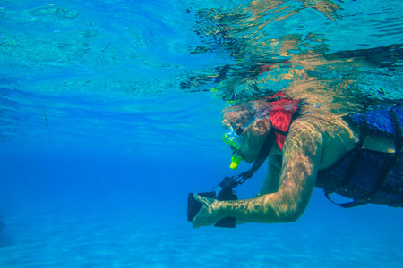 Man with photo camera taking photos and snorkeling underwater by coral reef in the Red sea, Egyptの写真素材