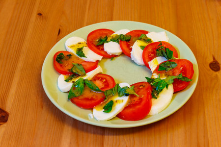 Italian caprese salad with tomatoes, mozzarella cheese and basil on a wooden tableの写真素材