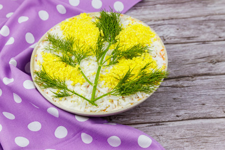 Traditional Russian layered salad Mimosa decorated with sprigs of mimosa (made of eggs yolk and dill) on wooden tableの写真素材