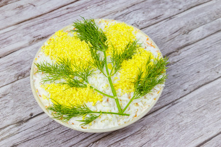 Traditional Russian layered salad Mimosa decorated with sprigs of mimosa (made of eggs yolk and dill) on wooden tableの写真素材