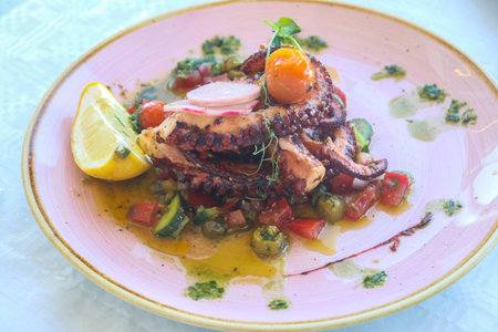 Delicious octopus dish served with lemon, vegetables and sauce in a restaurantの写真素材