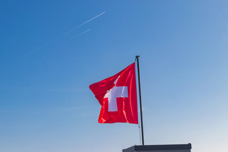 Red Swiss flag over the blue sky backgroundの写真素材