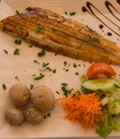 Fried plaice with canarian potatoes and vegetable salad on a plate