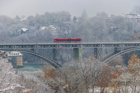 View to the Kirchenfeld bridge with running red bus on winter snowy day in Bern, Switzerland