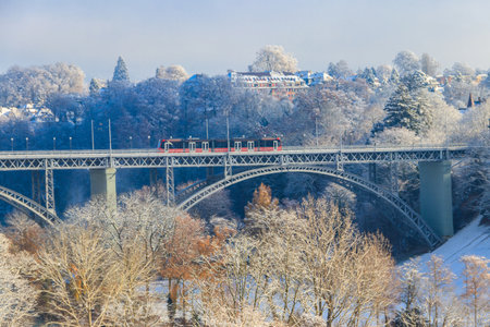 View to the Kirchenfeld bridge with running red tram on winter snowy day in Bern, Switzerland