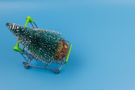 Shopping cart with Christmas tree on pastel blue background. Christmas shopping conceptの写真素材