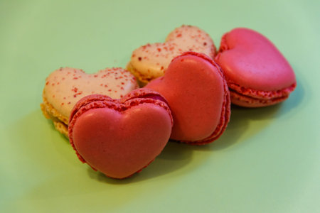 Sweet heart shaped macaroons on green background. Valentine Day concept