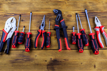 Set of different pliers and screwdrivers on wooden background. Top view
