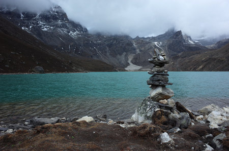Hiking in Nepal Himalayas, Stone pyramid next to Gokyo lake (4870 m) in beginning of summer. High altitude glacier lake in mountains in cloudy weatherの写真素材