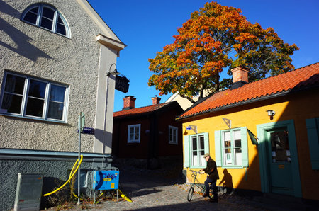 Vasteras, Sweden - 3 October, 2018: Sun is shining on small peaceful street with yellow house and red autumn color tree in old town of Vasteras cityのeditorial素材