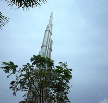 Dubai, UAE - April 12, 2019: Top of the Burj Khalifa skyscraper from behind tree, The tallest...