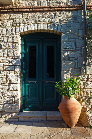 Pythagorion, Samos island, Greece - 13 May, 2018: Flowers in traditional clay vase next to wooden door and brick wallのeditorial素材