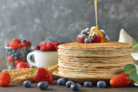 French crepes with berries and honey on a gray background