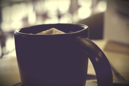 A black mug on background day light as bokeh rounds from window. Evening tea in the cafe. Tinted (toned) vintage imageの写真素材