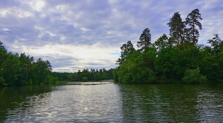 A beautiful green landscape with calm water surface. Reflection in the water forest, the blue sky and white clouds. Green grass in foreground.の写真素材