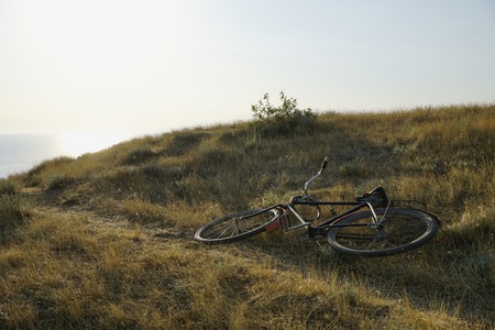 A vintage soviet iron bicycle lies on a yellow sun dried grass on the background of a sea surface in perspective and a bright scorching sunの写真素材