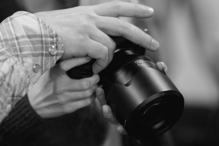 Close-up view of a man's and woman's hands with the newest camera with a large lens in his hands. Black and white image.の写真素材