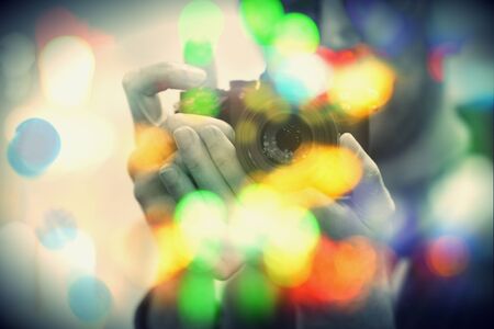 Close-up view of a man's hands with newest camera with lens in his hands. Bright round colorful circles outside focus in the frame in the foregroundの写真素材