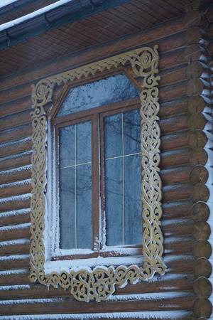 One window with light in a wooden house (church, temple) in a carved frame with snow on the windowsillの写真素材