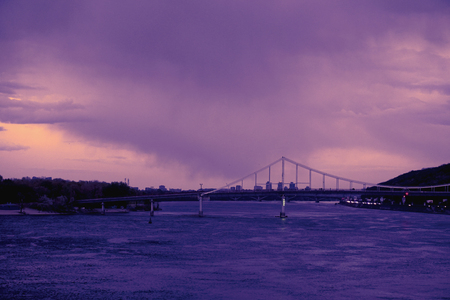 Bridge reflection in water surface of river Dnieper duaring sunset time. Toned image: purple, violet, yellow, orange colors.の写真素材