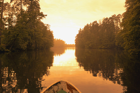 Forest reflection with boat on lake or river. Golden hour, orange sunset time.の写真素材