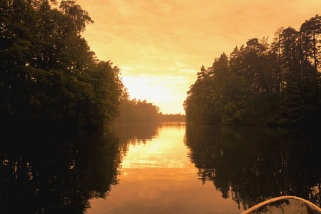 Forest reflection with boat on lake or river. Golden hour, orange sunset time.の写真素材