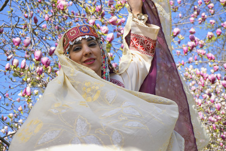 Pretty girl against of magnolia flowers in national Palestinian costume with head covered. Botanical garden.の写真素材