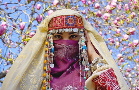 Pretty girl against of magnolia flowers in national Palestinian costume with head covered. Botanical garden.の写真素材