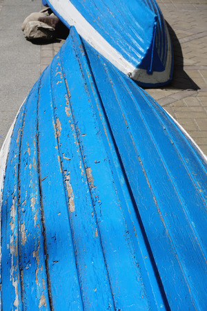 Old shabby blue and white two boats lie on the asphalt upside downの写真素材