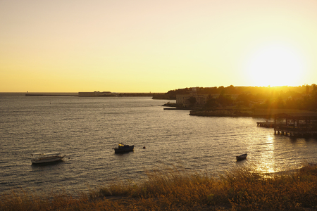 Black sea with fishing boats at yellow sunset time with bright sun. Sevastopol, Crimea, Russia.の写真素材