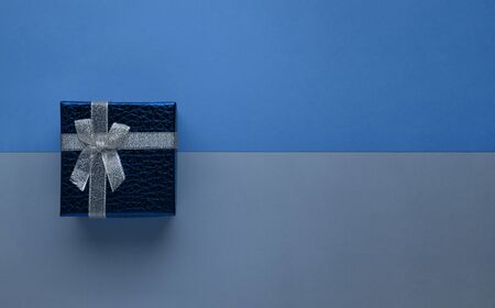 Blue gift box with silver bow on two-tone monochrome trendy classic blue paper background top view...