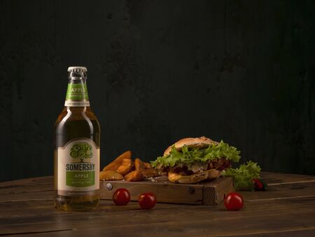 Somersby Apple Cider by Danish brewing company Carlsberg Group with fast food burger on a round wooden table. St.Petersburg, Russia. 2020-02-21.のeditorial素材