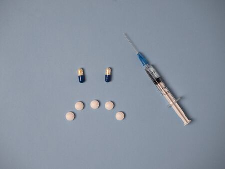 Syringe with medicine and sad smiley face made of blue and white medical pills on a blue background...
