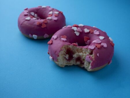 Bitten donut with berry filling on blue background. Two pink glazed donuts decorated with hearts.の写真素材