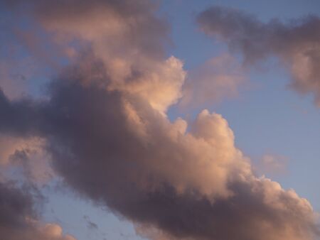 Gray-white thundercloud in a blue sky. Pink sky background at sunset.