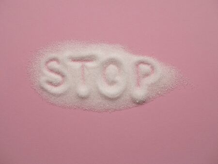 Heap of white sugar with word STOP hand written on it on a pink background top view. Stop diabetes and excessive sugar intake concept. Healthcare, unhealthy diet concept.の写真素材