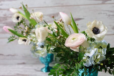 Two Bouquets of ranunculus, anemones and other fresh flowers in two blue vases stands on the background of vintage floor.の写真素材