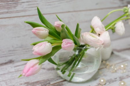 Tulips in a glass vase with water, standing on a light background or vintage wooden floor. View...