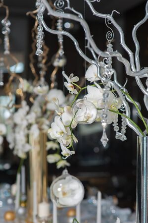 The branches of orchids in vases on the holiday table. Decorative branch with crystal elements decorated table.の写真素材