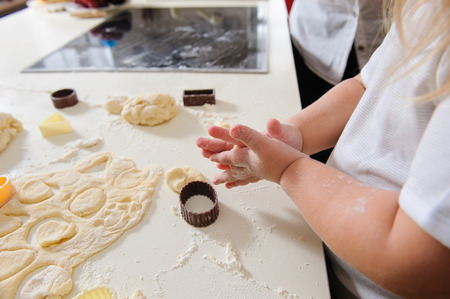 Children's hands knead the dough for baking cookies, dough, flour, baking tins on a white table in the background.の写真素材