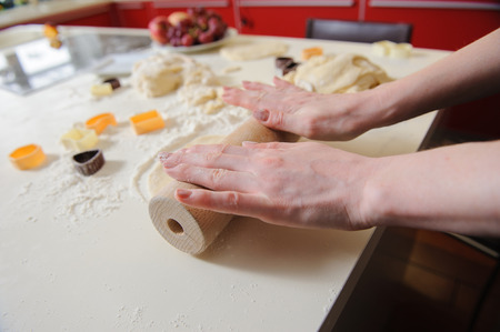 Hands of the child knead the dough in the kitchen. dough, flour, baking tins on a white table in the...