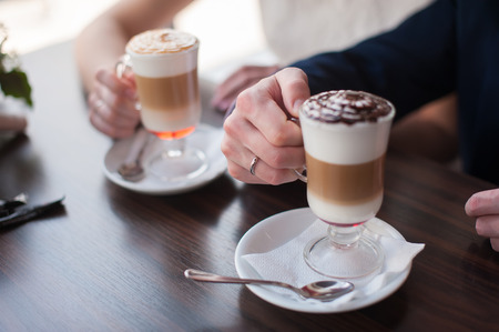 A man and a woman holding a cup of latte Women's and men's hands with wedding rings with two cups of coffeeの写真素材