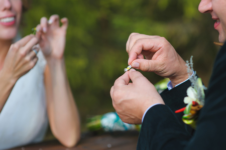 Guessing on the chamomile petals, bride and groom sit opposite each other and tear off daisy petals. focus on the hands of men. girl smiling, background is blurredの写真素材