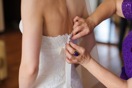 closeup portrait of a mom helping the bride with her dress in roomの写真素材