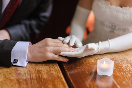 The groom holds the hand of the bride sitting at a wooden table.の写真素材