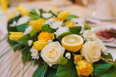 Beautiful holiday table setting with fresh flowers and half a lemon. close-up, white and yellow roses, tulips, green leaves.の写真素材