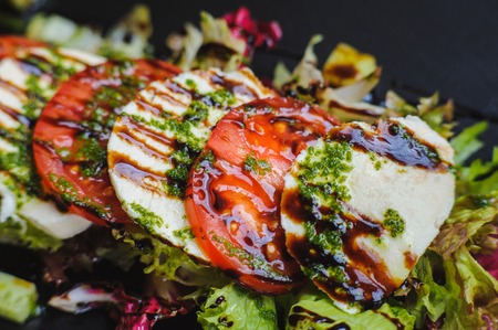 close-up Caprese - Italian salad with cherry tomatoes, olives and mozzarella cheese and basil on a black plate.の写真素材