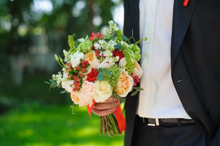 Groom in a black wedding suit holding a beautiful flowers bouquet.の写真素材